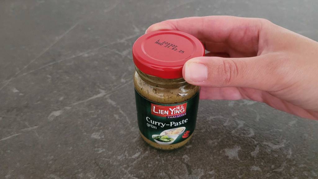 Eine Hand öffnet ein Glas Currypaste zum testen.