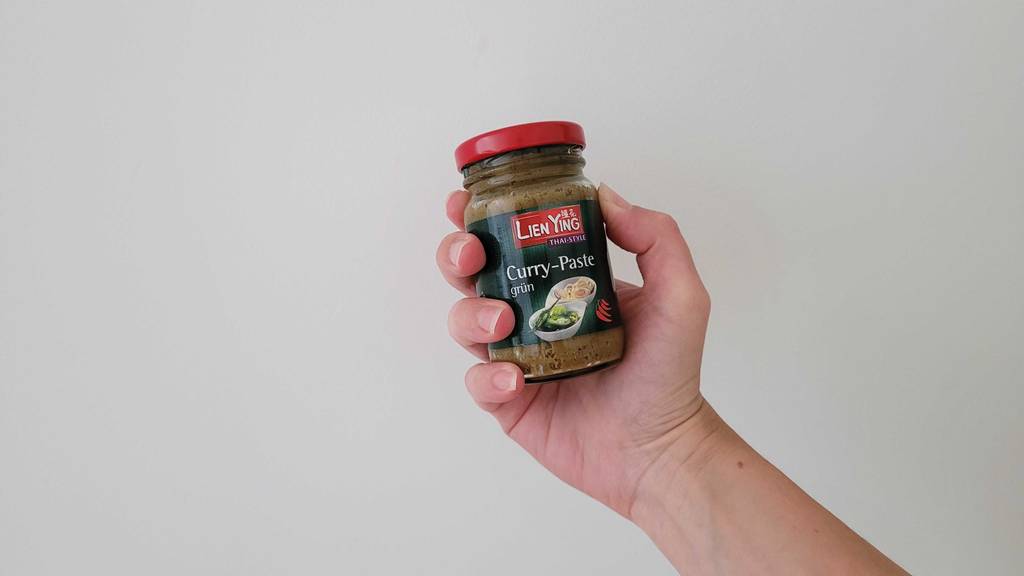 Im Test: Eine Hand hält ein Glas Currypaste vor einer weißen Wand.