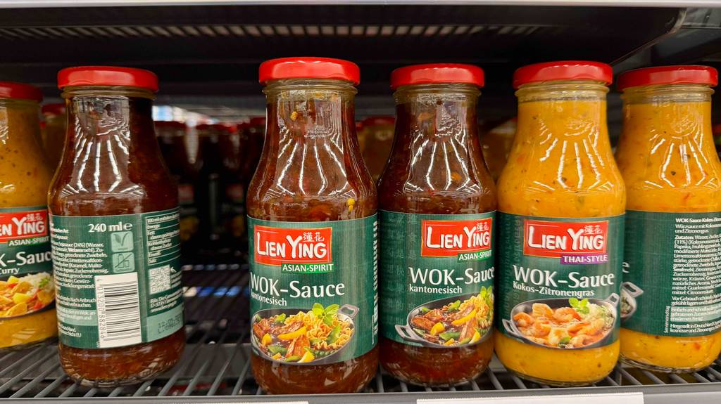 Mehrere Flaschen mit getesteter Wok-Sauce befinden sich nebeneinander in einem Verkaufsregal neben Soßen mit anderen Geschmacksrichtungen.