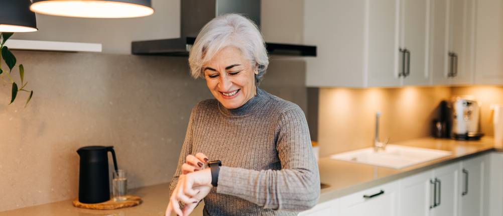 LIGE-Smartwatches im Test: ältere Dame, die in ihrer Küche lächelnd auf ihre Smartwatch schaut
