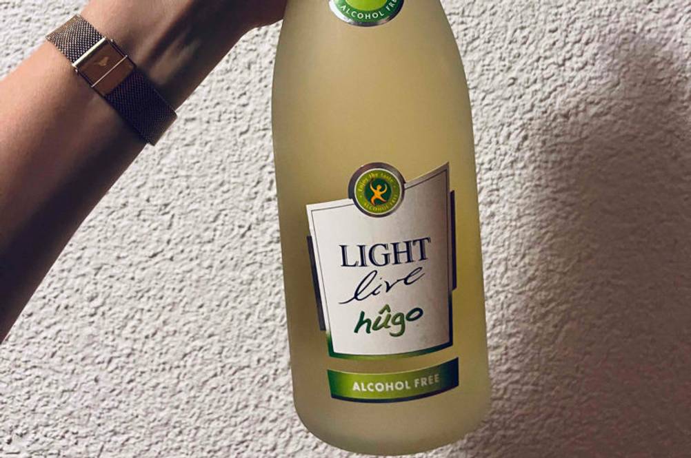 Alkoholfreier Sekt getestet: Hand hält eine Flasche Light Life Hugo vor weißer Wand.