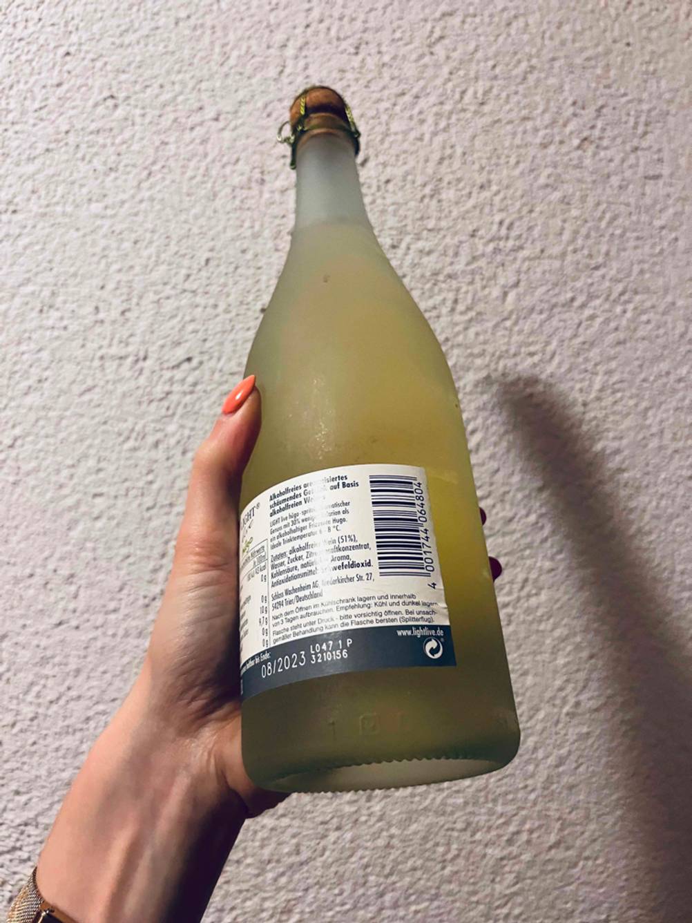 Im Test: Eine Hand hält die Rückseite einer Flasche alkoholfreien Sektes vor eine helle Wand.