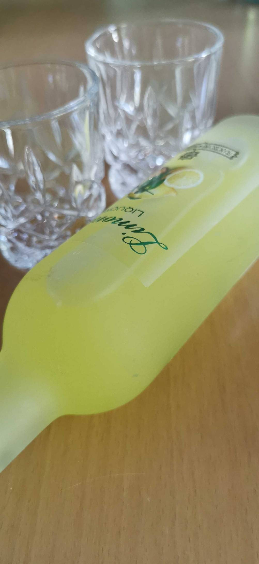 Limoncello getestet: Nahaufnahme der liegenden Flasche vor zwei Gläsern.
