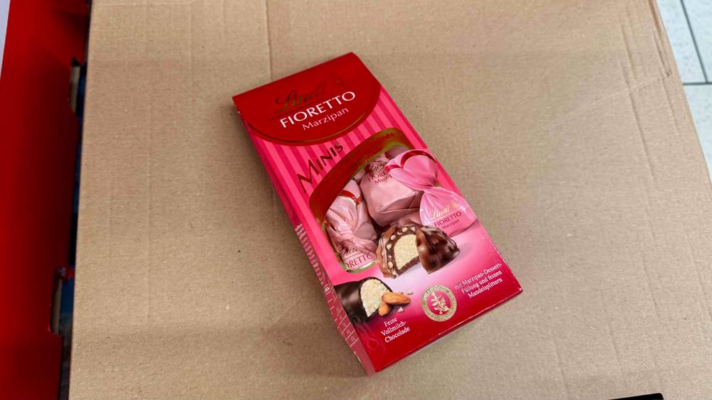 Auf einem Karton liegt eine Packung der getesteten Lindt-Pralinen.