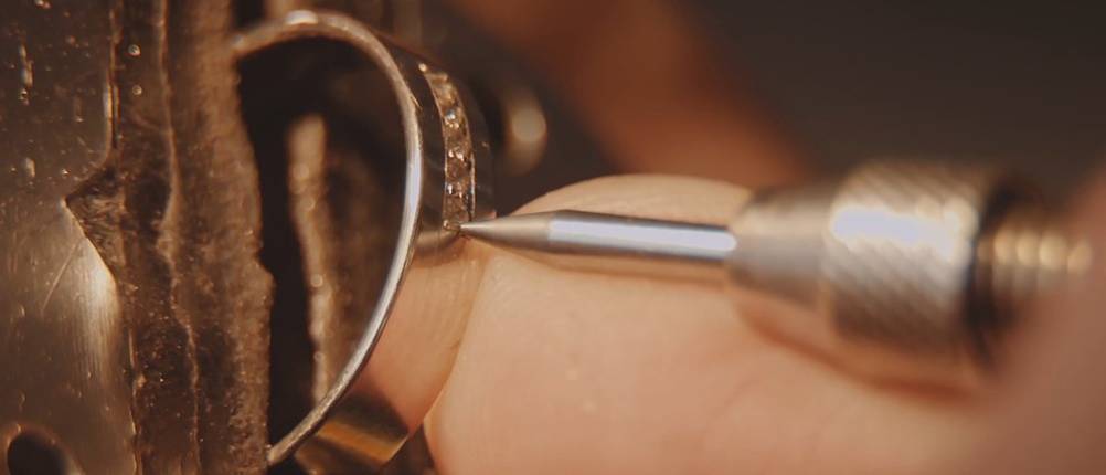 Im Bild ist zu sehen, wie eine Person eine Gravur an einem Goldring vornimmt.