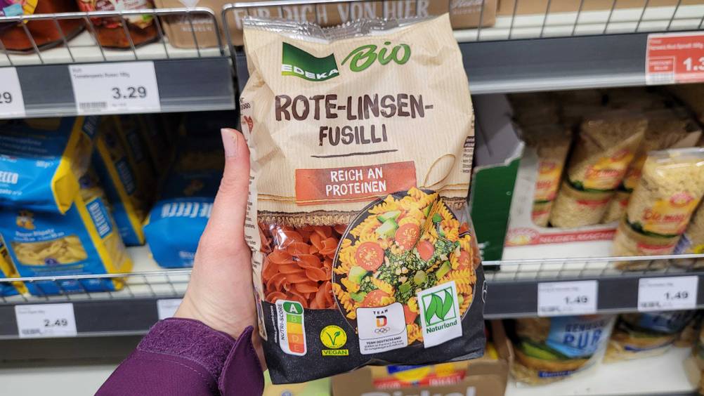 Eine Hand hält eine Packung der getesteten Linsennudeln vor ein Regal.