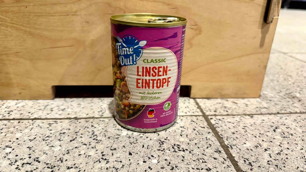 Eine Dose der getesteten Linsensuppe steht vor einer Holzbox am Boden.