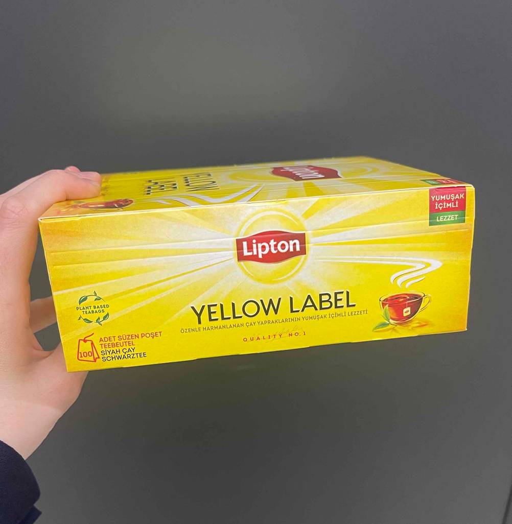 Eine Hand hält eine Packung getesteten Lipton-Tee in Seitenansicht.