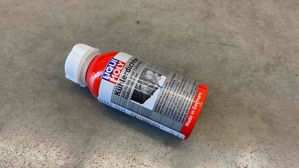 Eine rote Kunststoffflasche mit Liqui-Moly-Kühlerdichtmittel im Test liegt auf einem grauen Boden.