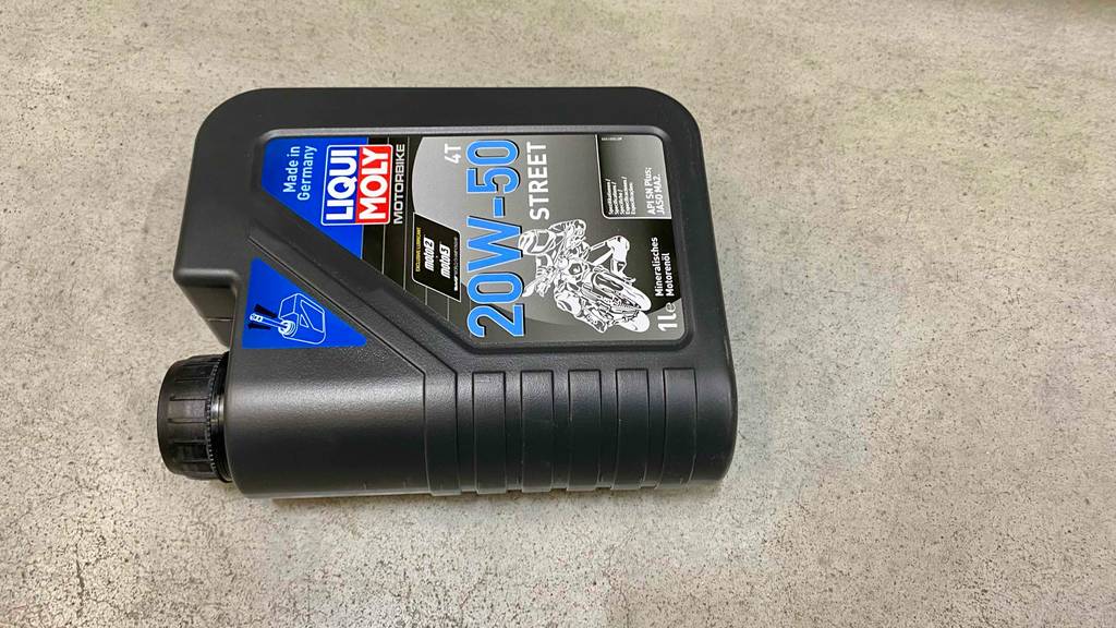 Im Test: 20w50-Motoröl der Marke Liqui Moly in einer anthrazitfarbenen 1-Liter-Kunststofflasche auf Zementboden liegend.