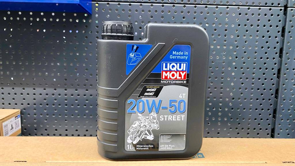 20w50-Motoröl-Test: eine anthrazitfarbene 1-Liter-Kunststofflasche steht vor einer grauen, gelochten Wand.
