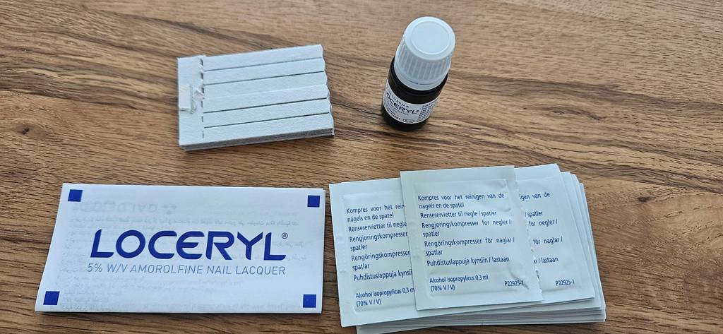Im Test: Mittel gegen Nagelpilz von Loceryl steht von oben betrachtet inklusive Produktanleitung und Anwendungszubehör auf einer Holzfläche.