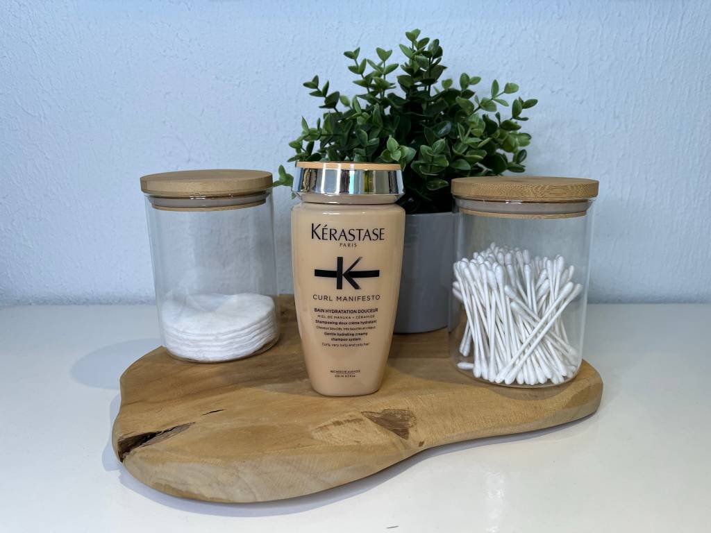 Locken-Shampoo steht auf Holztablett neben Wattestäbchen und Wattepads. 