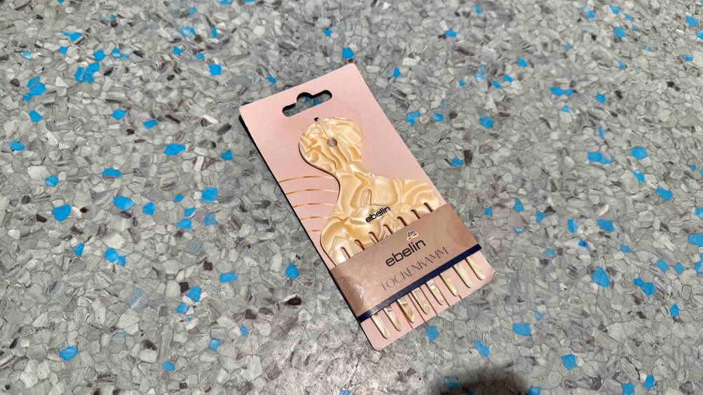Auf dem grau-blauen Boden liegt ein verpackter Lockenkamm im Test.