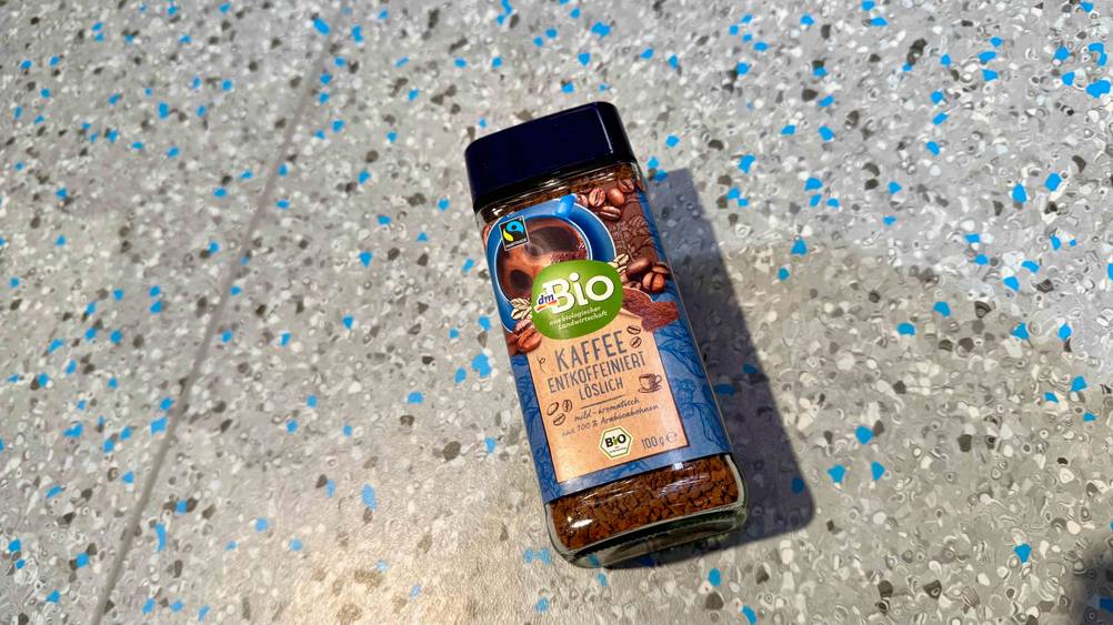 Auf dem grau-blauen Boden liegt eine Packung des getesteten löslichen Kaffees entkoffeiniert.