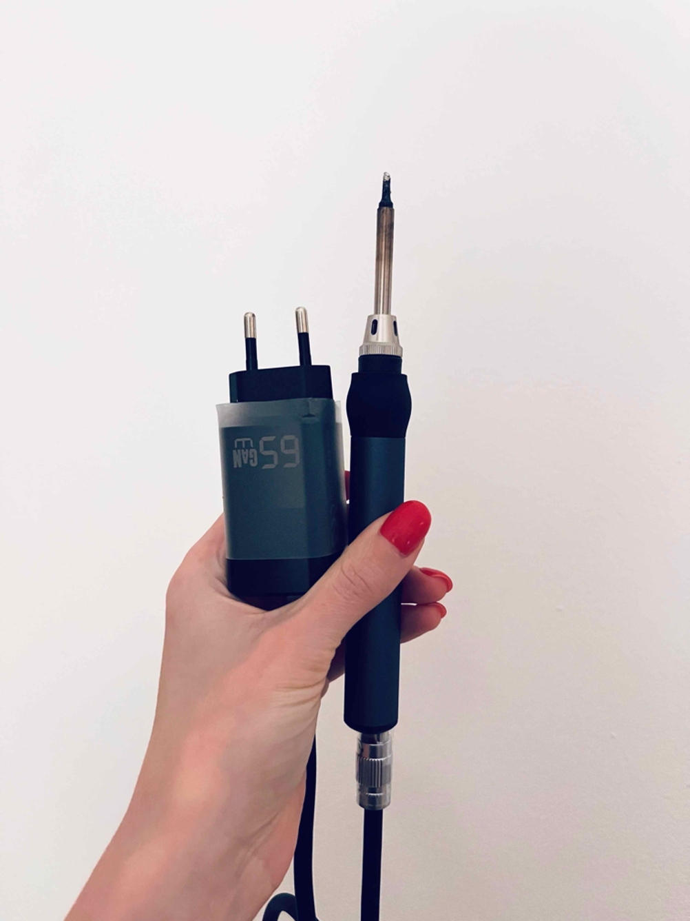 Im Test: Eine Hand hält einen Lötkolben und seinen Stromanschluss vor eine helle Fläche.