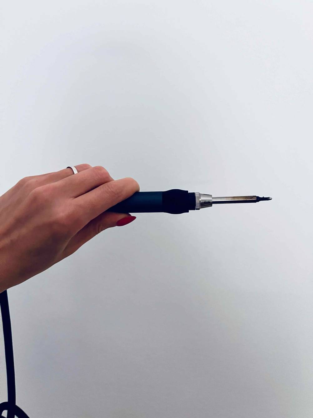 Eine Hand hält einen getesteten Lötkolben horizontal vor eine hellen Wand.