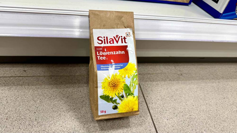 Vor einem Regal auf dem Boden steht eine Packung des Löwenzahntee im Test.