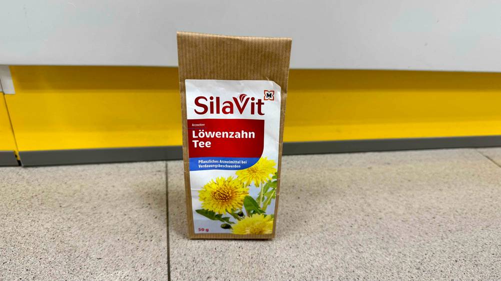 Der getestete Löwenzahntee steht vor einer hellen Fläche auf dem Boden.