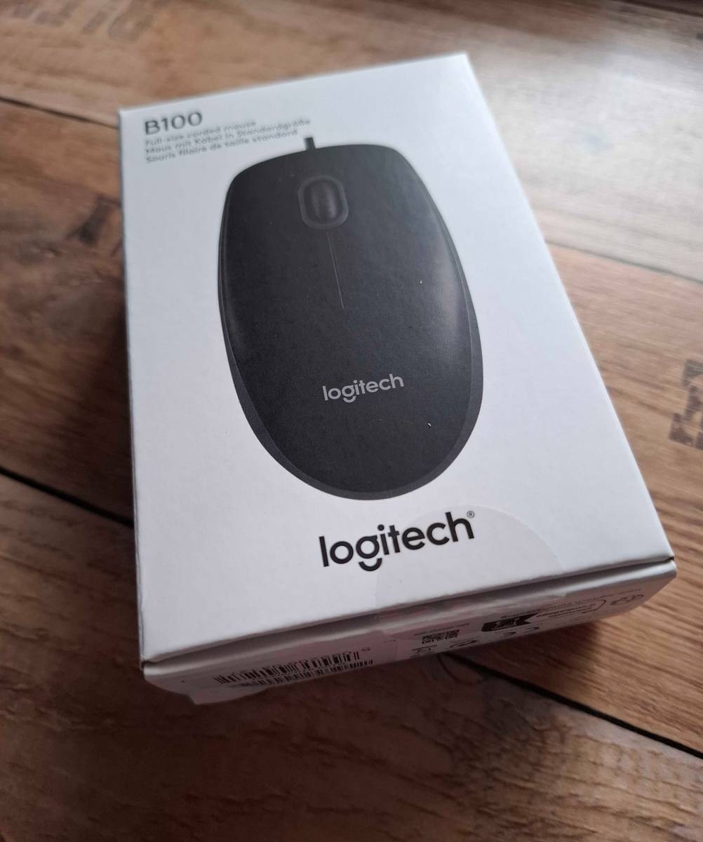 Der Originalverpackungskarton einer getesteten USB-Maus liegt auf einer Holzfläche.