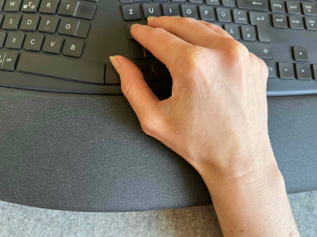 Eine Hand liegt von oben betrachtet auf dem Handgelenkkissen einer schwarzen, getesteten ergonomischen Tastatur.