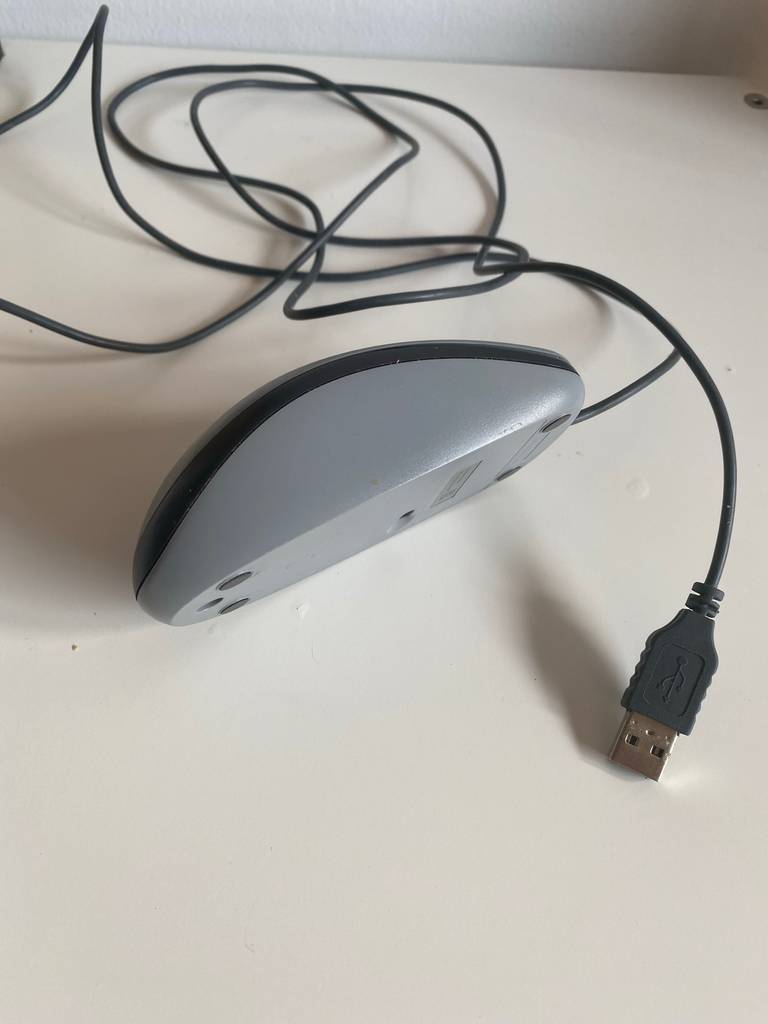 Logitech-Maus-Test: eine grau-schwarze Maus liegt inklusive USB-Kabel auf der Seite auf einem weißen Untergrund.
