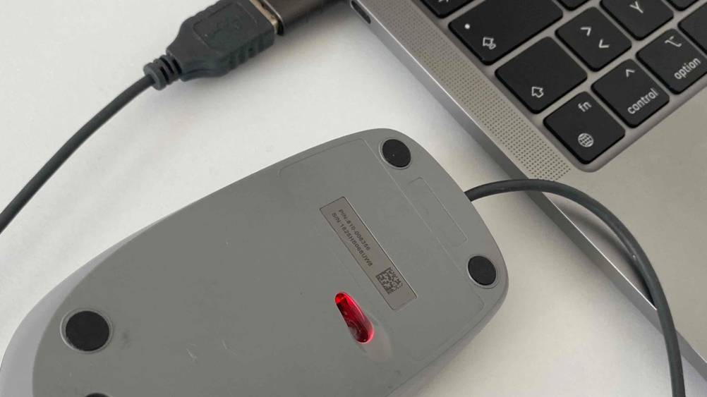 Nahaufnahme der Rückseite der getesteten Logitech-Maus mit Seriennummer neben einem Laptop.