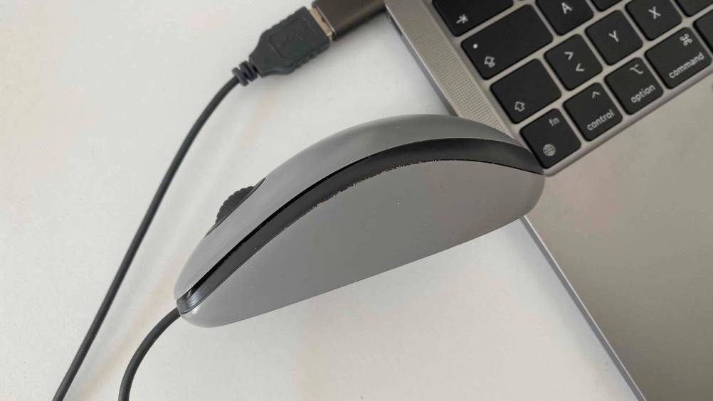 Seitenansicht einer getesteten Logitech-Maus angeschlossen neben einem Laptop auf einer hellen Fläche