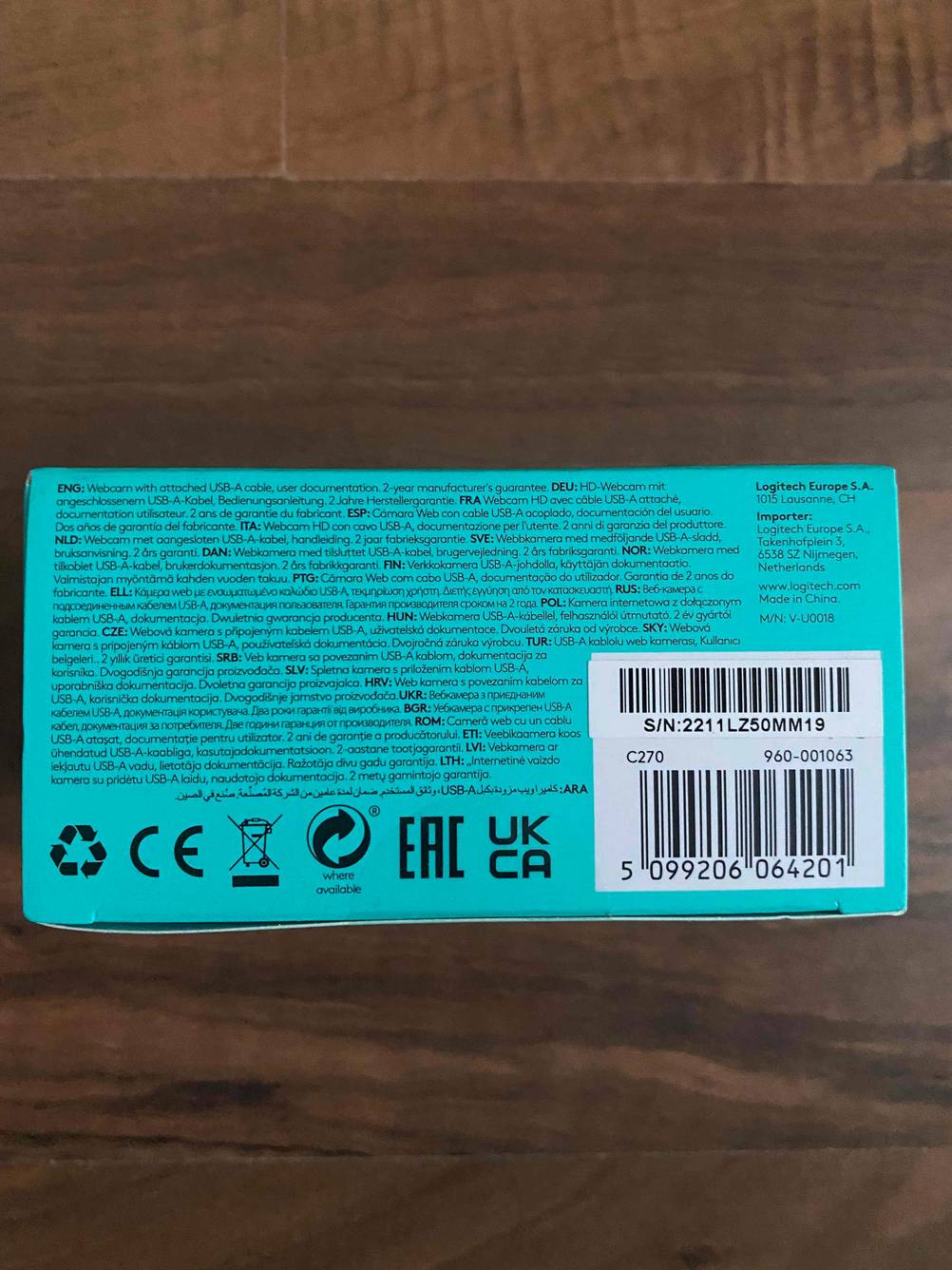 Im Test: Der Boden der Verpackung einer Logitech-Webcam mit Strichcode und Seriennummer auf einer dunklen Holzfläche.
