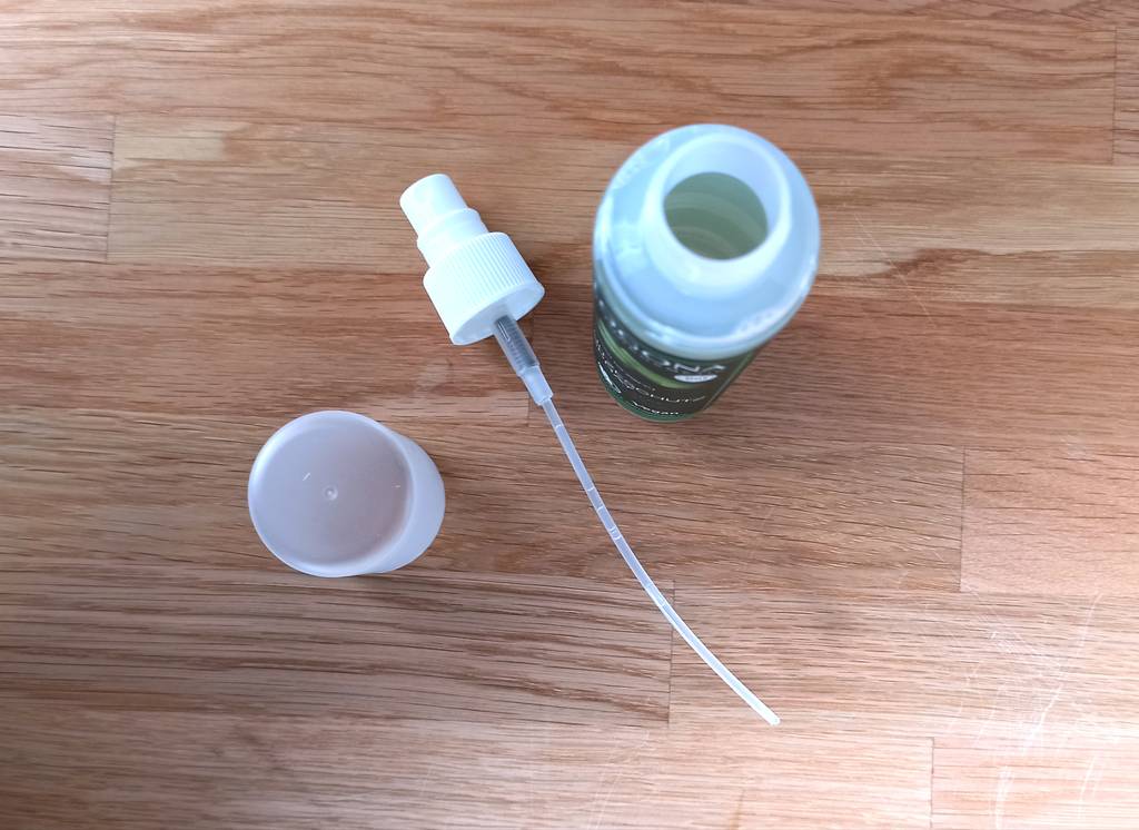 Ein auseinandergebautes Hitzeschutzspray, neben der leeren Flasche liegt der Deckel und der Schlauch für den Sprühmechanismus