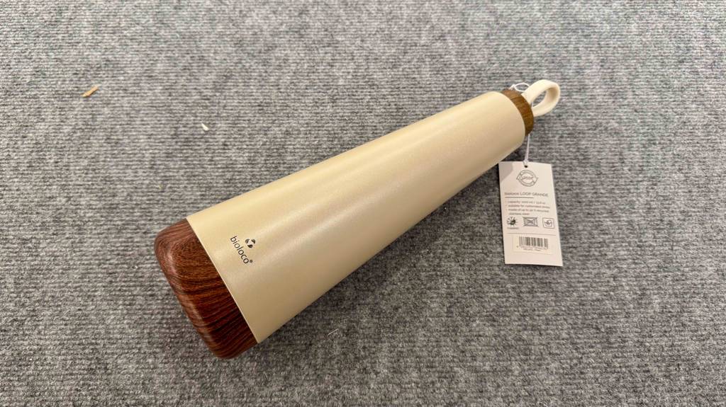 Eine getestete Edelstahl-Trinkflasche in Beige liegt auf einem grauen Stoffbelag.
