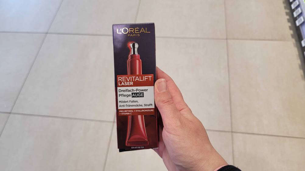 Eine Hand hält eine L'Oréal-Augencreme im Test hoch.