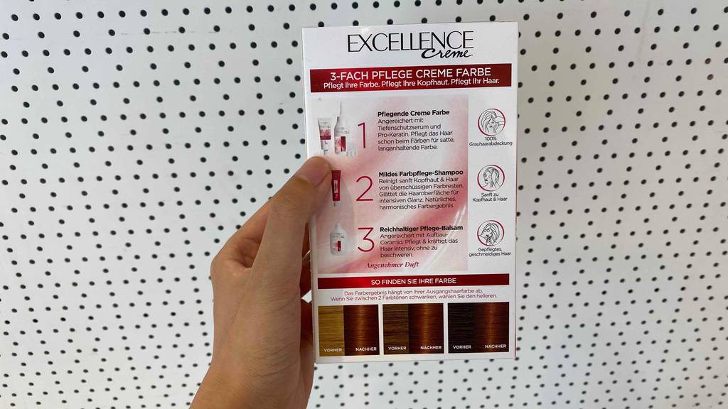 Getestet: Rückseite einer Packung L’Oréal Haarfarbe Excellence Creme wird von Hand vor weißer Lochwand gehalten.