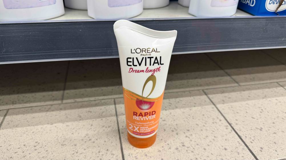 Vor einem Verkaufsregal am Boden steht eine Tube der getesteten L'Oreal-Haarkur.