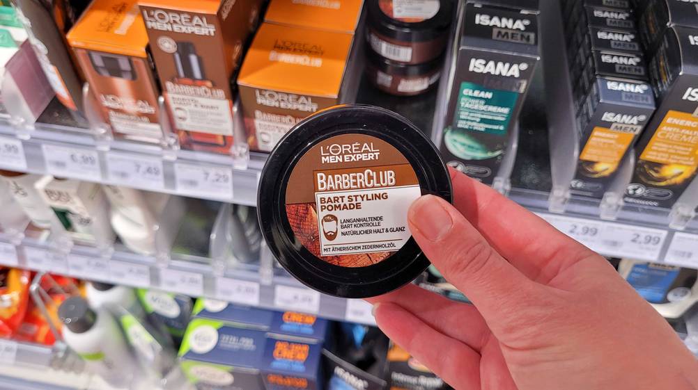 Eine Hand hält eine Dose der getesteten Pomade vor ein Regal mit Produkten.
