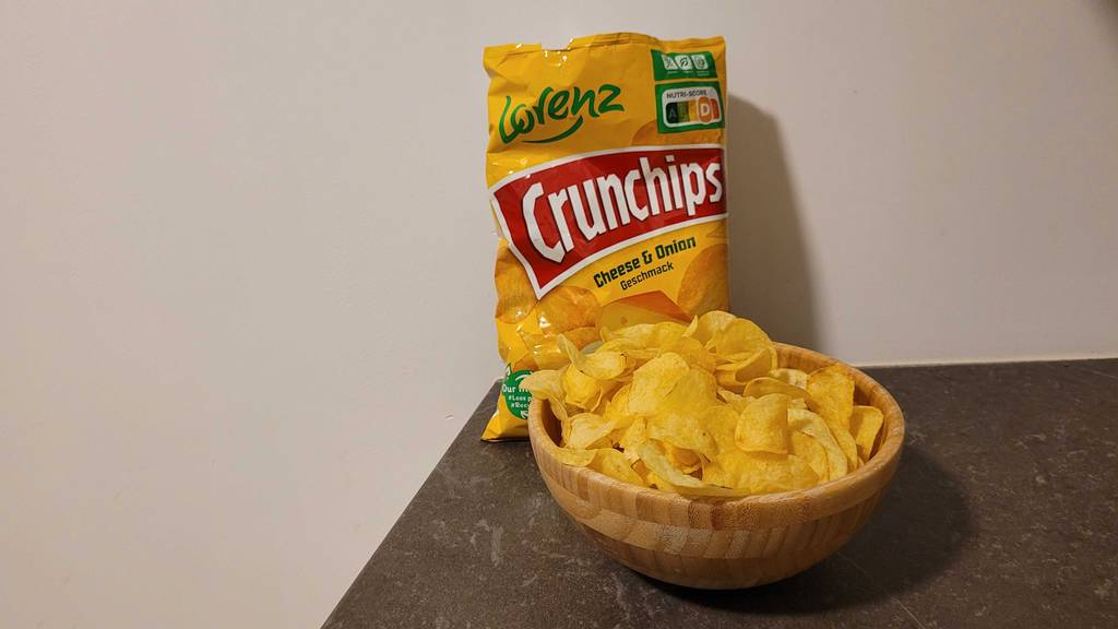 Eine Tüte Käsechips im Test steht hinter einer Holzschüssel mit Käsechips.