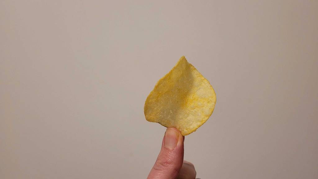 Zwischen zwei Fingern befindet sich ein Käsechip im Test.