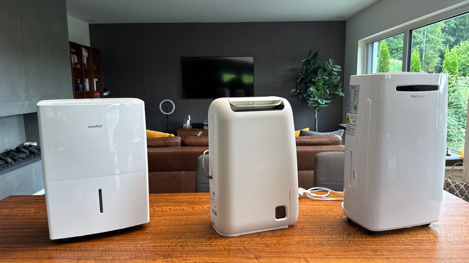 Drei Luftentfeuchter stehen nebeneinander auf einem Holztisch