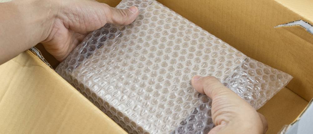 Luftpolsterfolie-Test: Hände legen einen in Luftpolsterfolie verpackten Gegenstand in ein Paket.