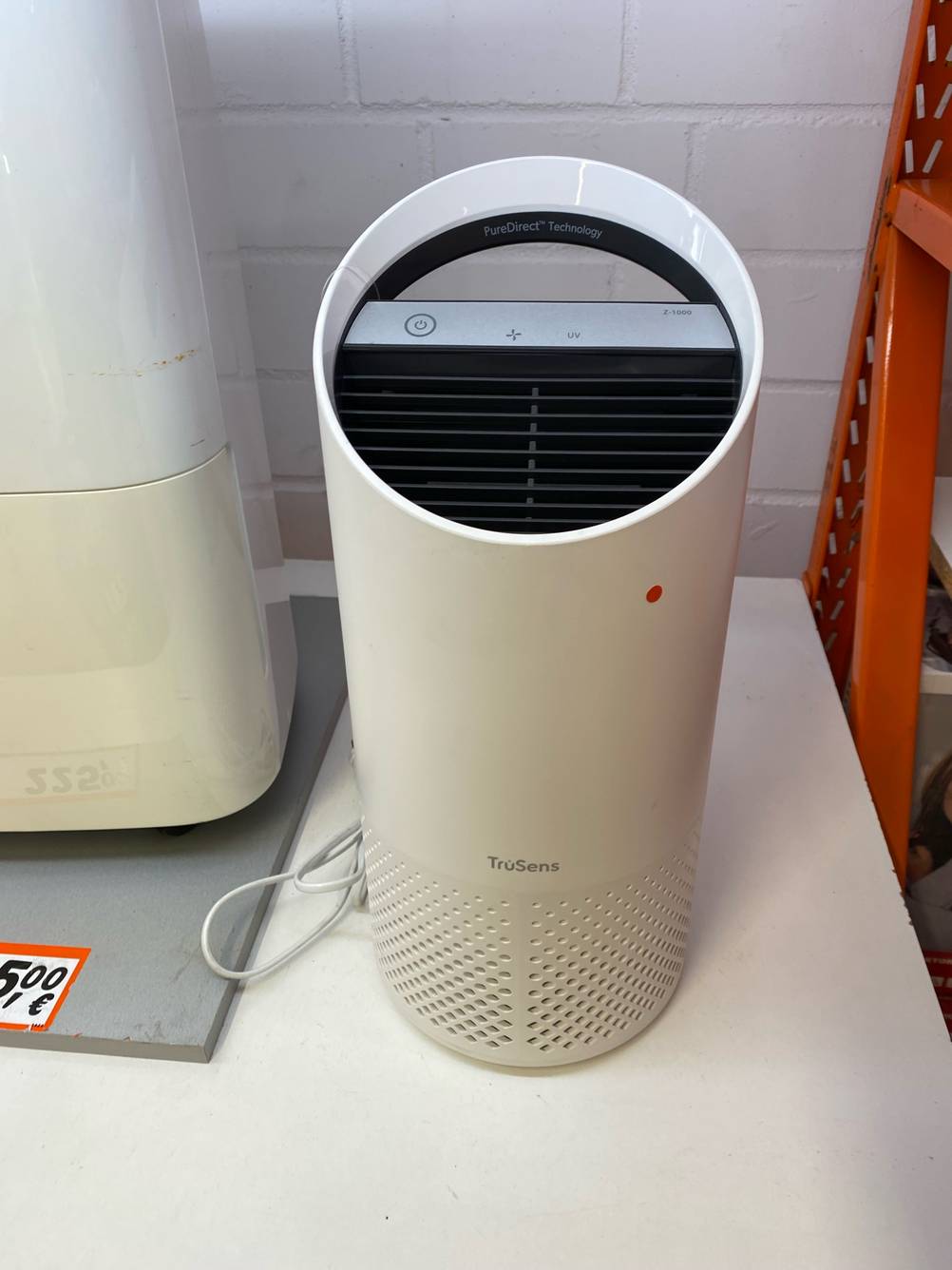 Im Test: Ein Luftreiniger von schräg oben auf einer hellen Fläche neben einem anderen Produkt.