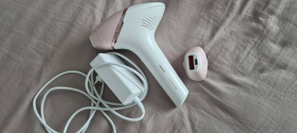 Im Test: IPL-Gerät von Philips in Weiß-Rosa liegt zwischen seinem Adapter und einem Aufsatz auf dunkelbeigem Stoff.