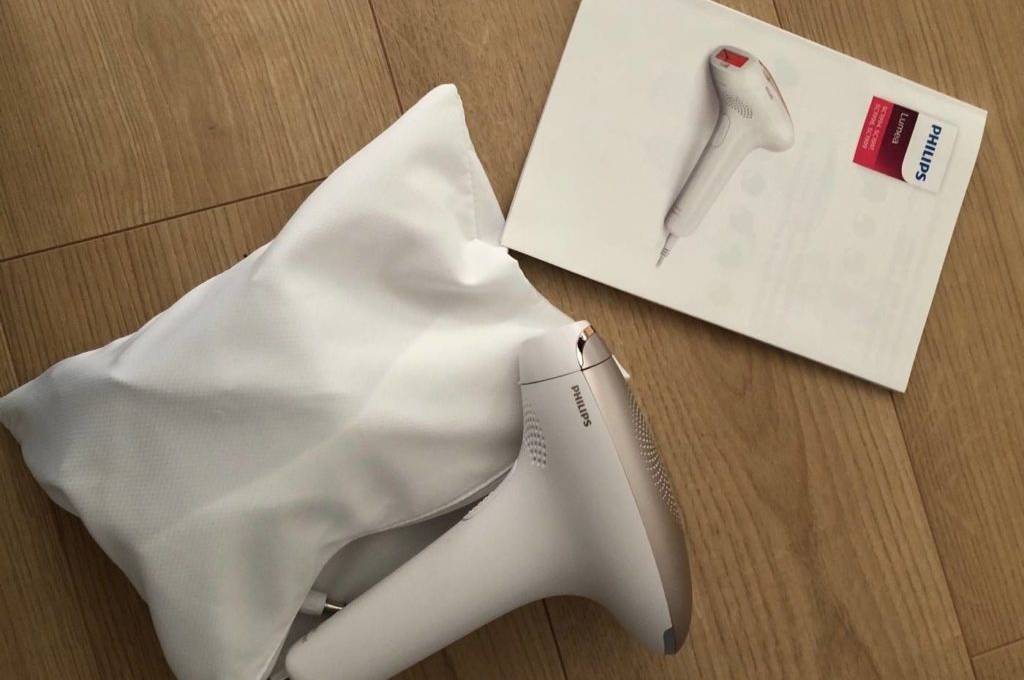 IPL-Geräte im Test: Philips Modell in Weiß-Rosa liegt außerhalb seiner weißen Aufbewahrungstasche neben der Bedienungsanleitung auf einem Holzboden.