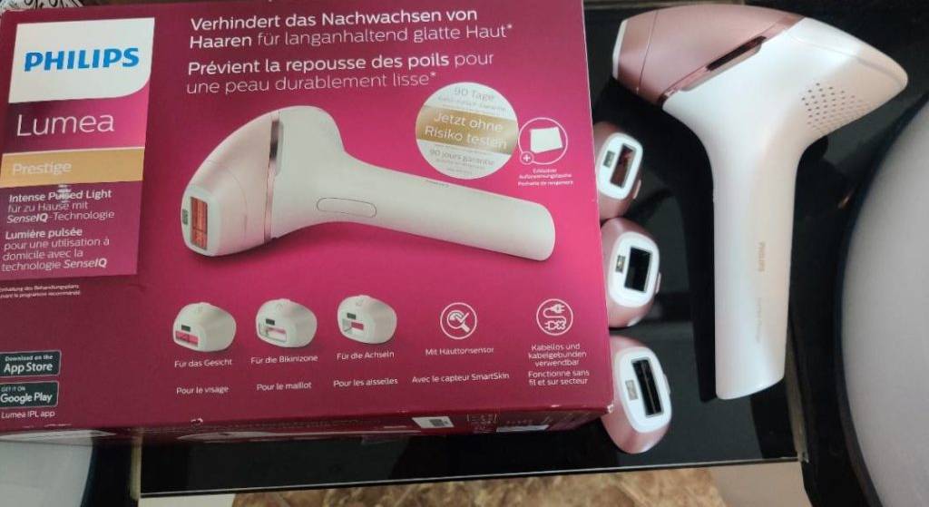 IPL-Geräte-Test: Philips Licht-Haarentfernungsgerät Lumea Prestige liegt neben drei verschiedenen Aufsätzen und seiner roten Originalverpackung.