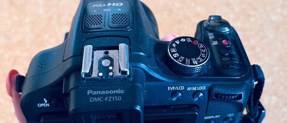 Digitalkamera-Test: Digitalkamera von Panasonic von schräg hinten, mit Blick auf schwenkbares Display, Blitzschuh und Einstellrad, in einer Hand gehalten