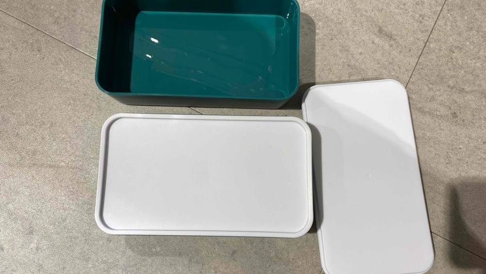 Alle Teile einer Lunchbox auf einer Fließenfläche nebeneinander liegend.