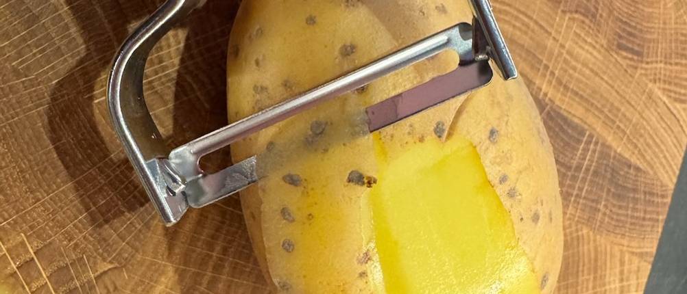 Eine Nahansicht der Sparschäler-Klinge, die eine Kartoffelschale entfernt.