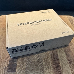 Der Karton des Lurch-10890-Butangasbrenner liegt auf einem Holzbrett