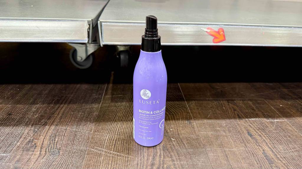 Ein lilafarbener Pumpspender mit Leave-in-Conditioner im Test steht vor einem Regal mit Rollen.