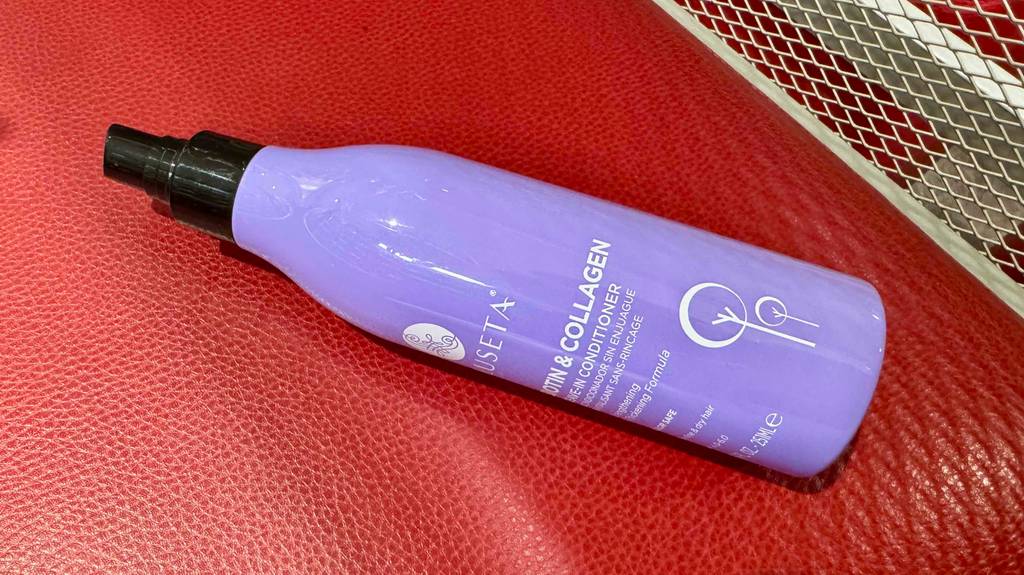 Getestet: Leave-in-Conditioner im lilafarbenen Pumpspender aus Kunststoff liegt auf einer roten Lederoberfläche.