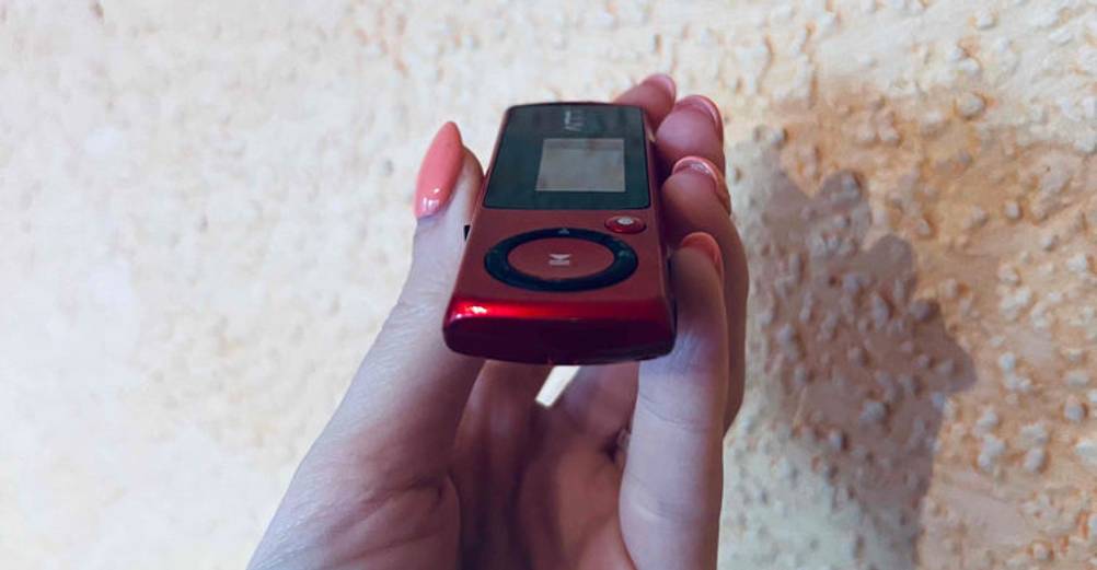 Hand hält einen dunkelroten MP3-Player im Test, mit Fokus auf die schmale Seite vor einer weißen Raufasertapete